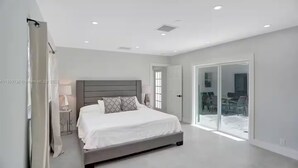 Een moderne slaapkamer met een groot bed, een nachtkastje en een schuifdeur naar een balkon.