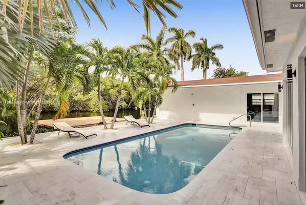 Una piscina con sillas de descanso, rodeada de palmeras y un edificio moderno.