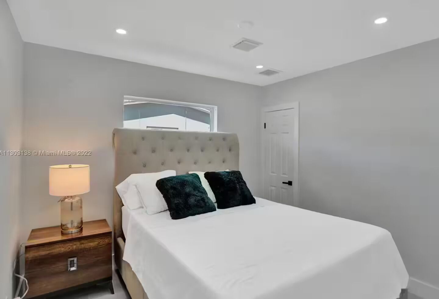 A bedroom with a bed, a nightstand, a lamp, and a door.