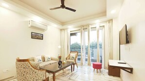 A living room with a sofa set, a coffee table, a TV mounted on the wall, and a ceiling fan. - Barrier-free apartment  Fortis (Gurugram)