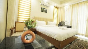A hotel room with a bed, a desk, a chair, a vase with flowers, and an air conditioning unit. - Barrier-free apartment  Fortis (Gurugram)