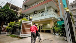 Un edificio a più piani con ingresso chiuso da cancello, piante in vaso e una persona che spinge una carrozzina.