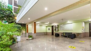 Spaziosa hall con soffitto alto, reception, area salotto e ampia finestra con vista sul verde.