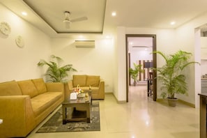 A living room with two sofas, a coffee table, and a ceiling fan. - Parfait Street 2Bhk service apartment near Fortis (Gurugram)
