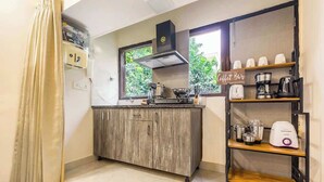 A compact kitchen with a wooden cabinet, a coffee bar with various appliances, and a window providing a view of greenery outside.
