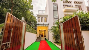 A modern building with a red carpet leading to a yellow entrance, surrounded by greenery.