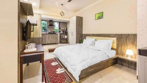 A bedroom with a bed, bedside table, lamp, ceiling fan, and a view into the kitchen.