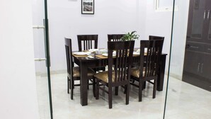 A dining area with a glass partition, a table set with plates, a plant, and framed pictures on the wall. - Parfait Street 3Bhk Service Apartment Near Fortis (Gurugram)