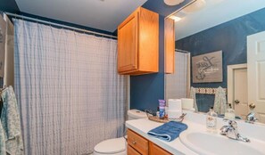 A bathroom with a shower curtain, a toilet, a sink with toiletries, and wooden cabinets.