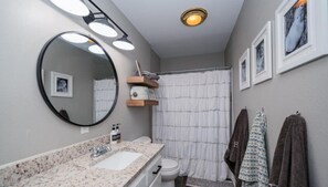 A bathroom with a sink, mirror, and toilet. There are towels hanging on the wall and a shower curtain.