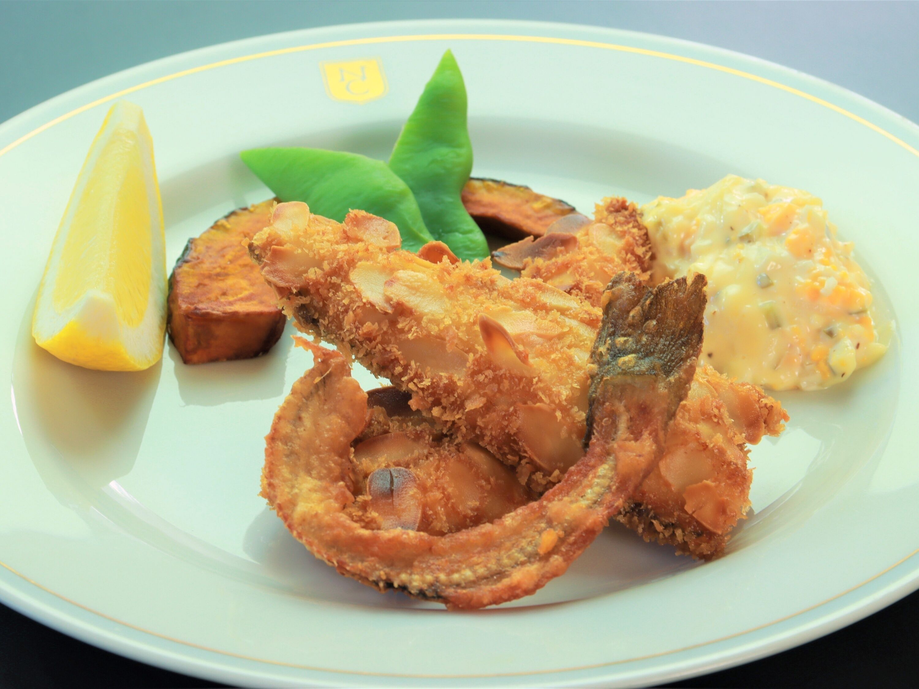 A plate with fried fish, a lemon wedge, and a side of mashed potatoes.