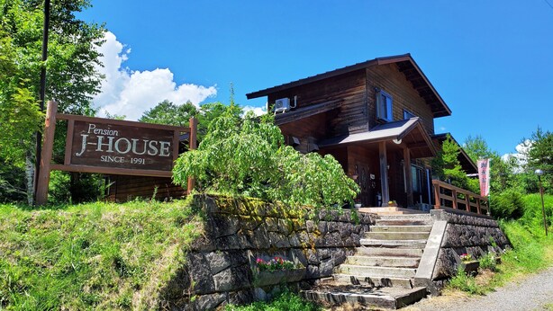 A wooden J-House with a stone staircase leading to the entrance, surrounded by greenery. - Pension J-HOUSE (Kiso)