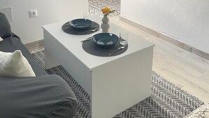 Ein modernes Wohnzimmer mit einem weißen Sofa, einem Couchtisch mit zwei blauen Tellern und einer Vase sowie einem an der Wand befestigten Fernseher.