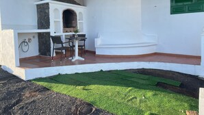 Eine Terrasse im Freien mit einem Steinofen, einem Tisch mit Stühlen und einem kleinen Gartenbereich.