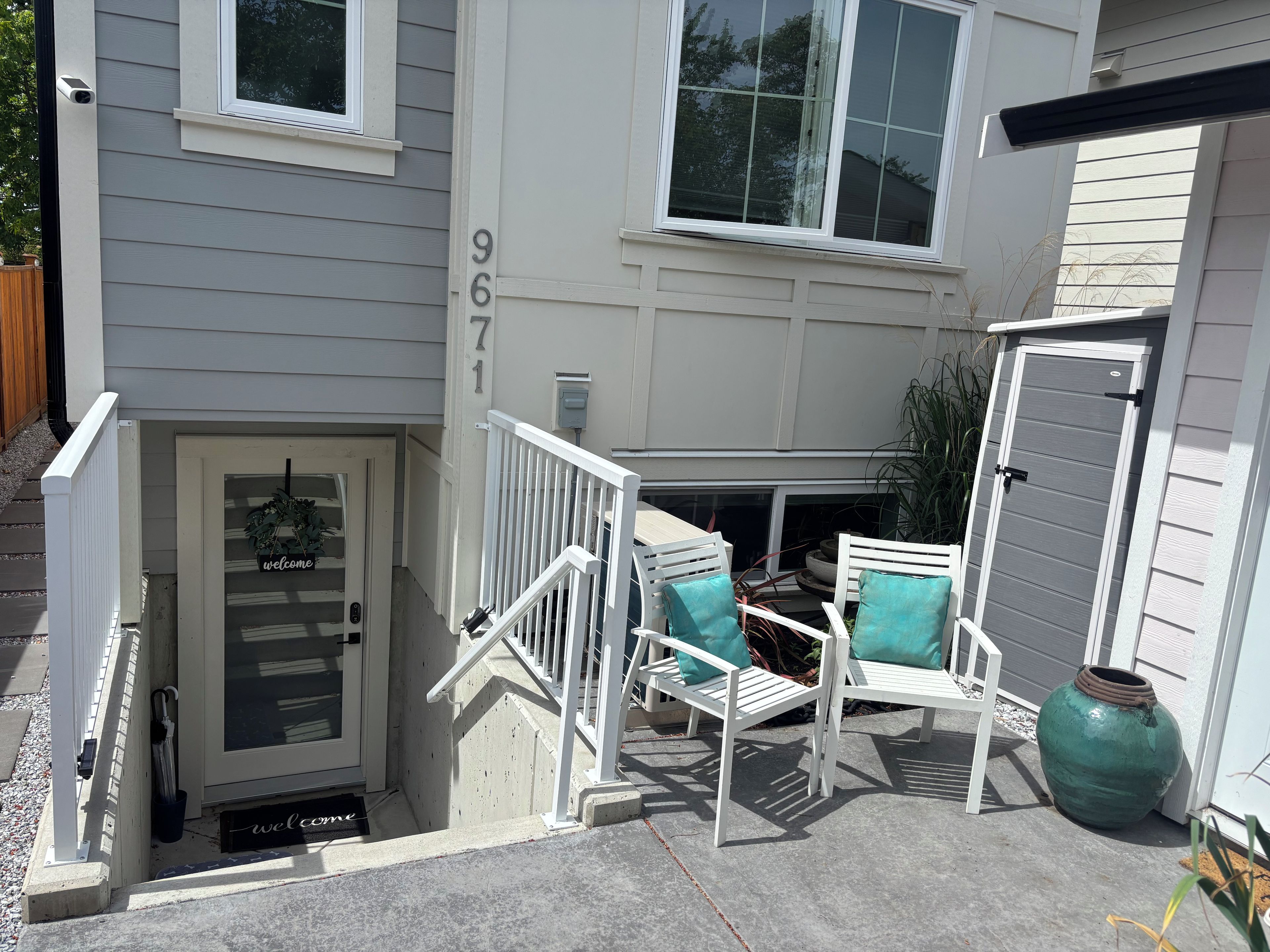 Un acceso residencial con puerta, escalones y un pequeño espacio al aire libre con sillas.