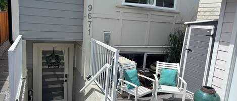 Un acceso residencial con puerta, escalones y un pequeño espacio al aire libre con sillas.