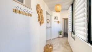 A hallway with a tiled floor, a wooden coat rack, decorative wall art, and a woven light fixture. - Funchal Panoramic View, a Home in Madeira (Funchal)