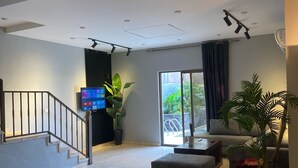 A modern living room with a dining area, a staircase, and a large window with a view of greenery. - San Vito chalet (Sweimeh)