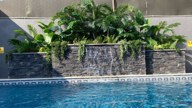 A swimming pool with clear blue water, surrounded by stone walls and lush green plants. - San Vito chalet (Sweimeh)