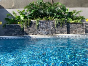 A swimming pool with clear blue water, surrounded by stone walls and lush green plants. - San Vito chalet (Sweimeh)