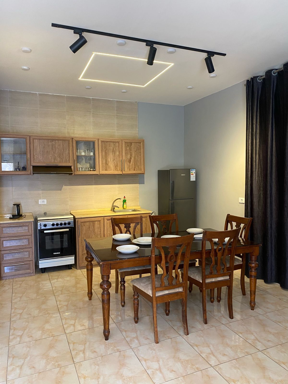 A modern kitchen with wooden cabinets, a gas stove, a refrigerator, and a dining table with chairs.