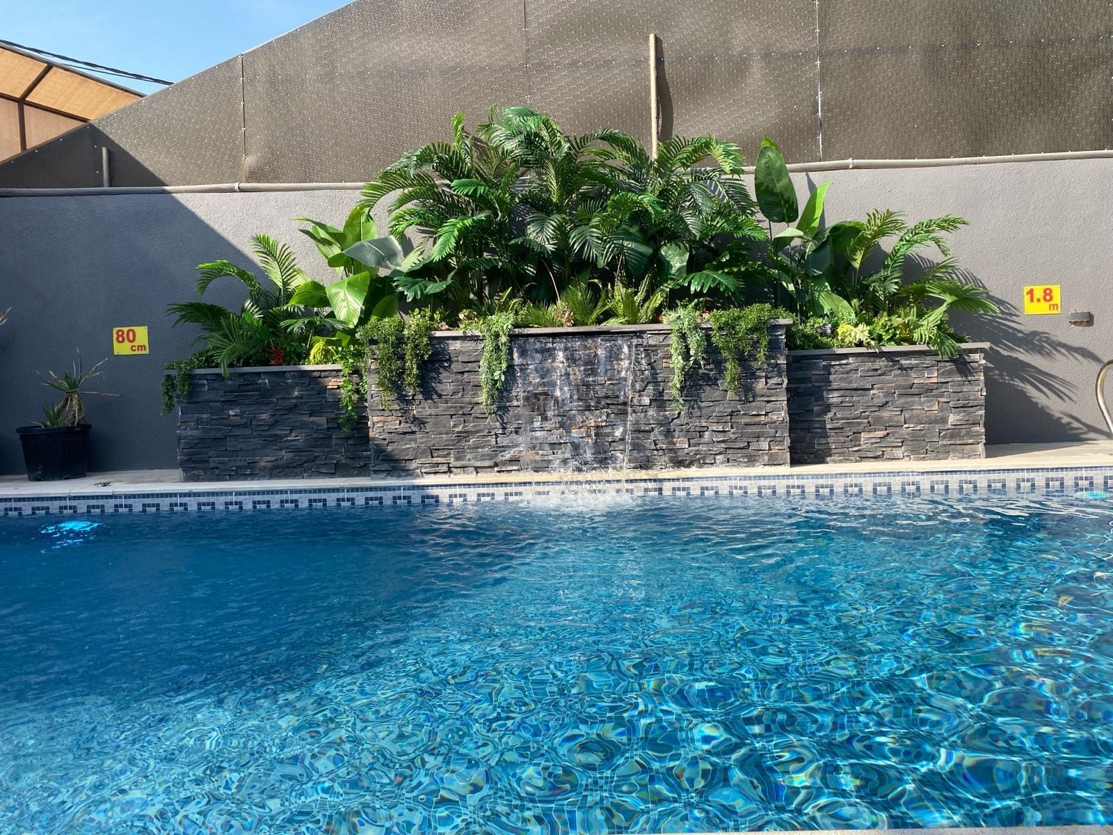 Una piscina con agua azul cristalina, rodeada de muros de piedra y exuberante vegetación.