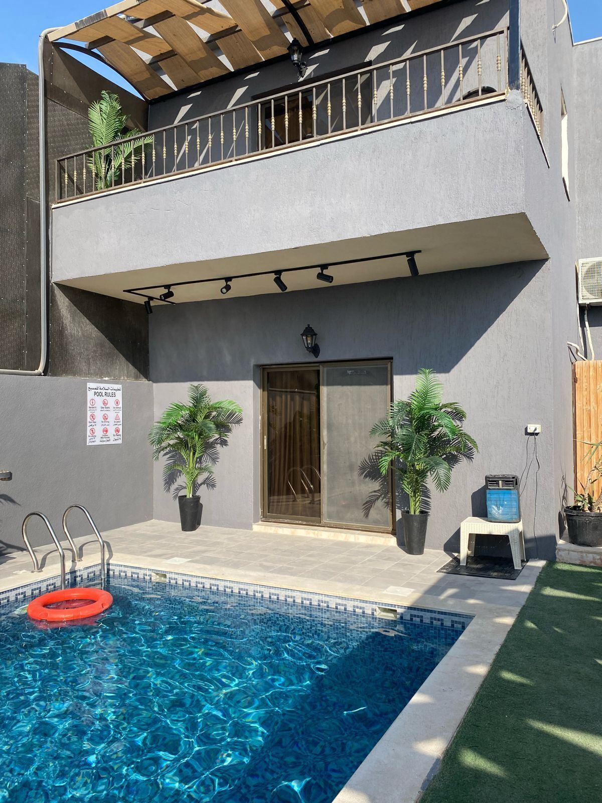 A two-story building with a swimming pool, potted plants, and a balcony.