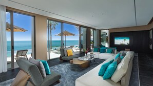 A modern living room with a large window overlooking the ocean, furnished with sofas and a coffee table, and a flat-screen TV mounted on the wall. - The Aquila Villa  (Kamala)