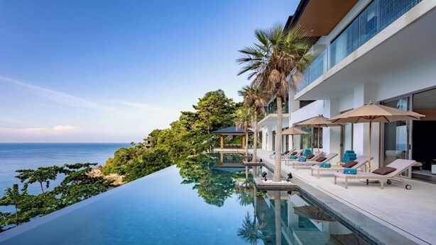A modern infinity pool with clear blue water, lounge chairs, and umbrellas, overlooking a lush green landscape and the sea. - The Aquila Villa  (Kamala)