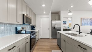 A modern kitchen with white cabinets, stainless steel appliances, and a large island with a sink. - El Gato 2 Bedroom Condo (Hurricane)