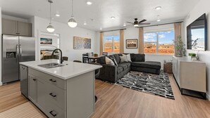 A modern kitchen with a central island, dining area with a sofa, and large windows offering a desert view. - El Gato 2 Bedroom Condo (Hurricane)