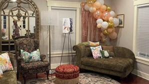 Una sala acogedora con un sillón floral, un reposapiés estampado y un sofá verde.