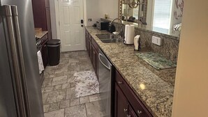 Una cocina con encimeras de granito, un refrigerador de acero inoxidable, un ventilador de techo y una ventana con persianas.