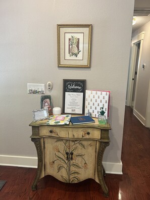 A wooden console table with a framed welcome sign, a framed pineapple artwork, and a birthday card. - "Bess" in Park Circle, North Charleston
 Family Friendly (North Charleston)
