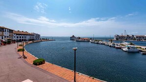 Un puerto deportivo con barcos amarrados, un paseo marítimo pavimentado y edificios con balcones.