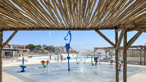 Zona de juegos acuáticos al aire libre con múltiples chorros de agua y una piscina, rodeada por una pérgola de madera.
