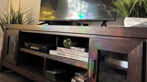 A wooden entertainment center with a flat-screen TV, a decorative hanging light, and a small plant.