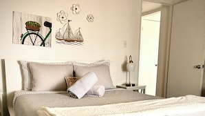 A neatly made bed with a white comforter and pillows, a bedside lamp, and a wall with a bicycle and flower decorations.