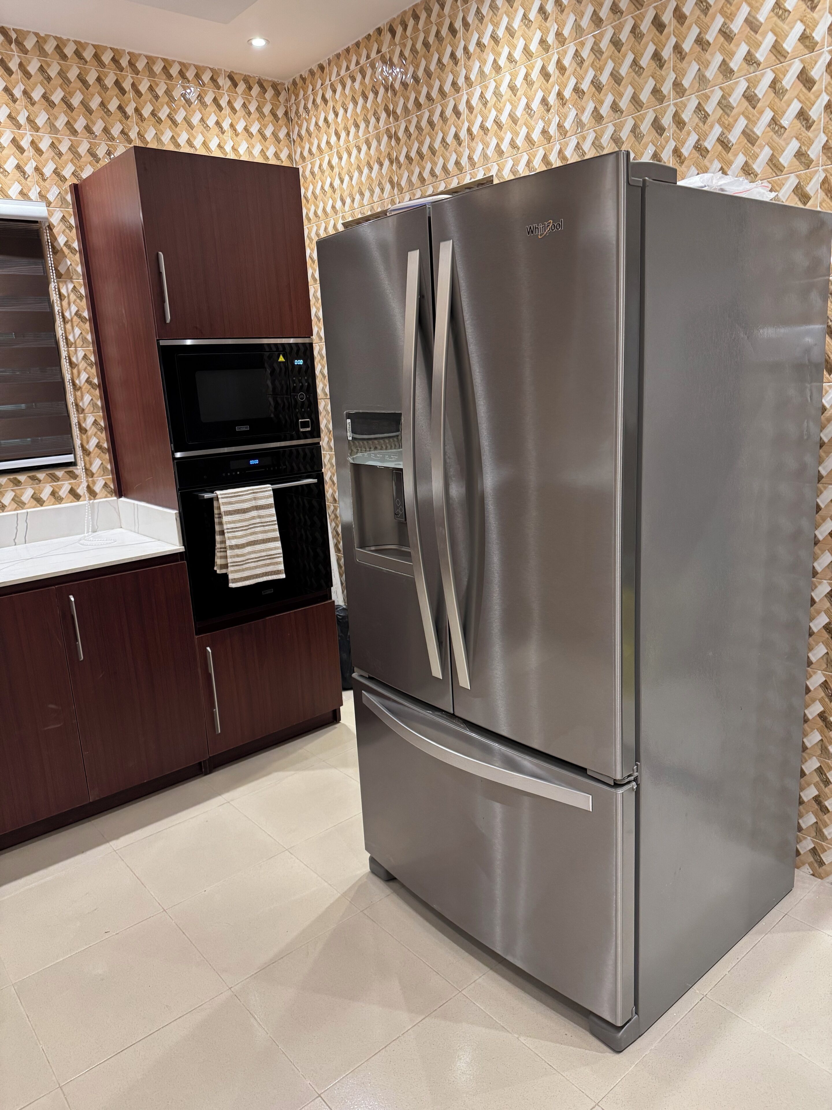 Eine Küche mit einem Edelstahl-Kühlschrank, einer Mikrowelle und Holzschränken.