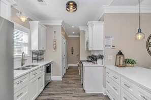 A kitchen with white cabinets, a wooden floor, and a hanging light fixture.