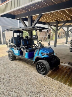 A blue golf cart parked under a covered area with a gravel surface.