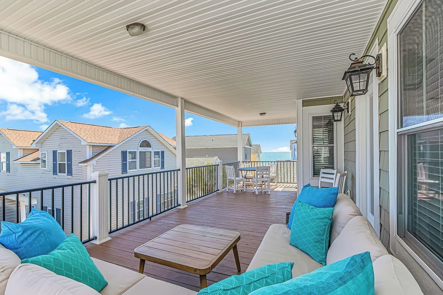 A covered porch with a wooden deck, outdoor furniture, and a view of neighboring houses.