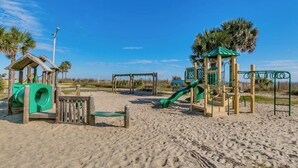 A sandy beach with a playground featuring slides and climbing structures. - Ocean Views! 5BR Beach House Steps to Beach! (Myrtle Beach)