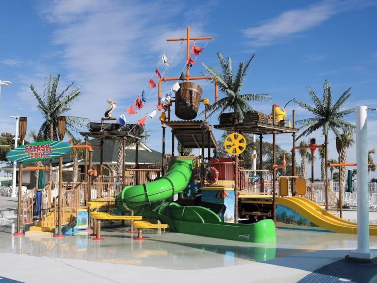 Un parc aquatique avec un toboggan vert, une structure de jeux sur le thème des pirates et un espace réservé aux jeux d’eau.