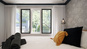 A hotel room with a large window, a bed with a white quilt, a black pillow, a mustard-colored throw, and a rolled-up towel on the floor. - Alf and Lisa's Luxury Glebe House - 2BR, 2BA With Free Lockup Parking (Glebe)