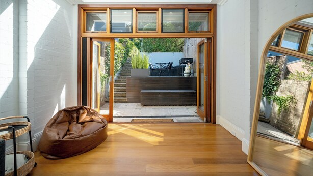 A room with a wooden floor, a bean bag, a wicker chair, and a view through a glass door to an outdoor area with steps and greenery. - Alf and Lisa's Luxury Glebe House - 2BR, 2BA With Free Lockup Parking (Glebe)