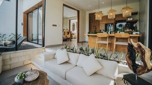 A modern living room with a sofa, a wooden coffee table, and a large window. - Villa Manna Ubud (Ubud)
