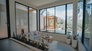 A modern living room with large windows, a wooden pergola, and a white sofa. - Villa Manna Ubud (Ubud)