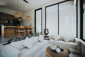 Una sala de estar moderna con un sofá blanco, una mesa de centro de madera y una zona de cocina con armarios de madera y una barra.