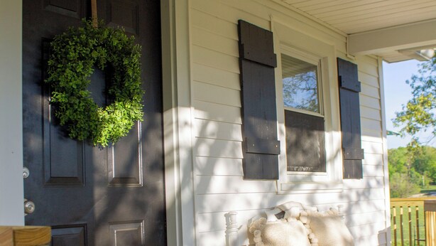 A porch with a dark door, a white bench with cushions, and a potted plant.